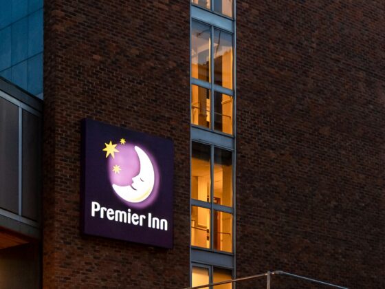 Brick building at dusk with a vertical row of lit windows and a glowing Premier Inn sign outside.