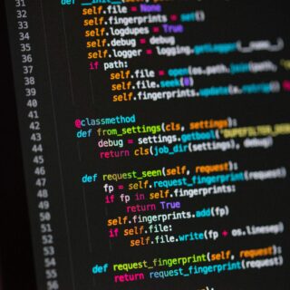 Close-up of a dark monitor showing colorful Python code with def and self. highlighted syntax appears in pink, orange, blue, and green.