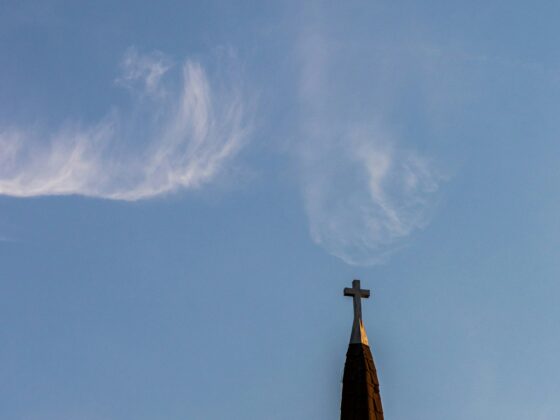 Church steeple with a cross at the top against a clear blue sky with wispy clouds (lower right).