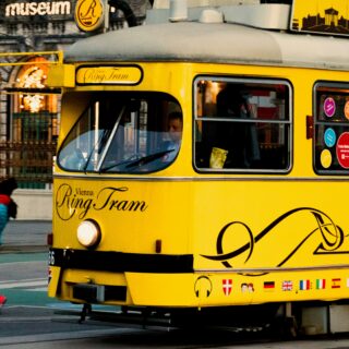 Bright yellow Vienna Ring Tram with windows showing passengers, parked on a city street as pedestrians walk by.