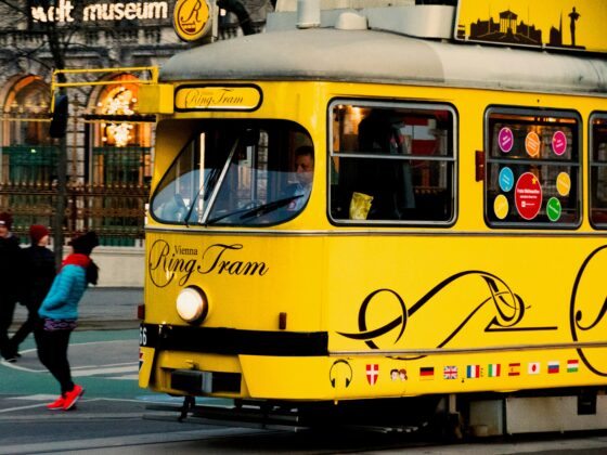 Bright yellow Vienna Ring Tram with windows showing passengers, parked on a city street as pedestrians walk by.