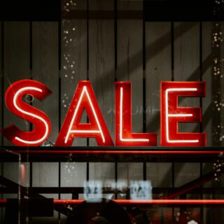 Red neon letters spell 'SALE' against a dark wooden backdrop in a storefront window.