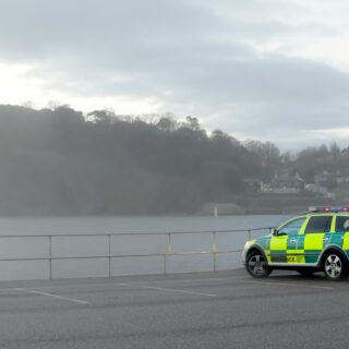 Ambulance car parked by a seaside promenade with a cliff and calm water in the background on a cloudy day