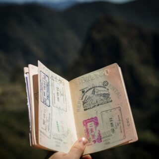 Open passport displaying colorful visa stamps held outdoors, with a blurred natural background.