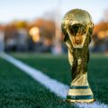 Gold trophy planted on a green sports field beside a white line, close-up shot in warm autumn light.