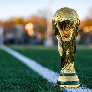 Gold trophy planted on a green sports field beside a white line, close-up shot in warm autumn light.