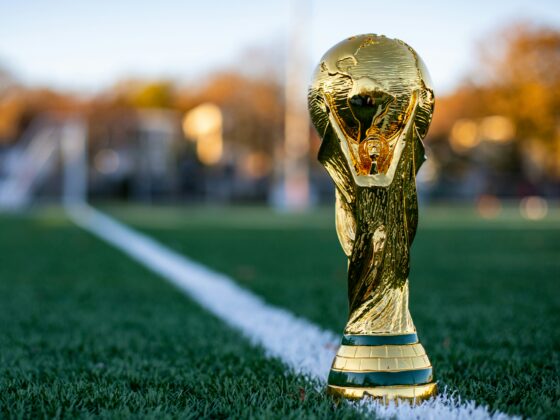 Gold trophy planted on a green sports field beside a white line, close-up shot in warm autumn light.