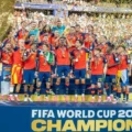 Spain national football team celebrating on the podium with medals as confetti falls, after winning FIFA World Cup 2026 (banner reads Champions).