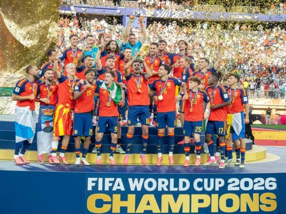 Spain national football team celebrating on the podium with medals as confetti falls, after winning FIFA World Cup 2026 (banner reads Champions).