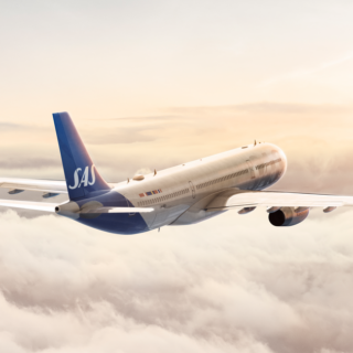 Side view of a SAS commercial jet flying above fluffy clouds at sunset.
