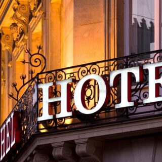 Hotel sign on an ornate building balcony at dusk, large white letters spell 'HOTEL'