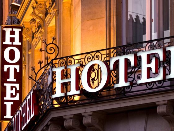 Hotel sign on an ornate building balcony at dusk, large white letters spell 'HOTEL'