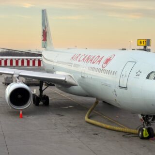 Air Canada aircraft parked at gate with jet bridge, ground hose and orange cones on tarmac at sunset