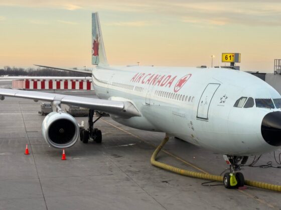 Air Canada aircraft parked at gate with jet bridge, ground hose and orange cones on tarmac at sunset