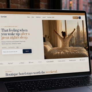 Laptop screen shows a hotel booking site (Sonder) with a person stretching in bed beside a city view; a coffee cup sits on the table nearby.