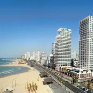 Modern white glass skyscrapers beside a sunny beach and blue ocean at a coastal city edge.