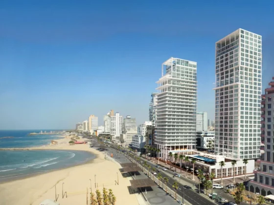 Modern white glass skyscrapers beside a sunny beach and blue ocean at a coastal city edge.