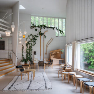 Bright, airy interior with white walls, wooden seating, and large windows framed by greenery a calm gathering space.