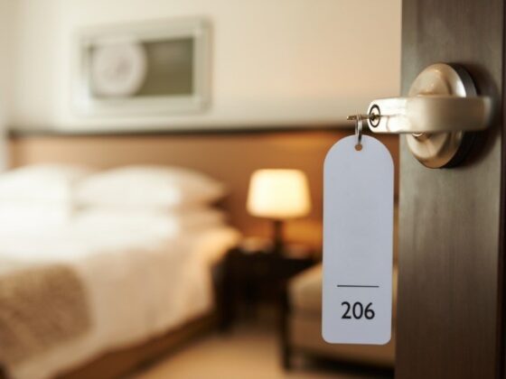 Hotel room door with key tag reading 206, blurred bedroom and lamp in the background.