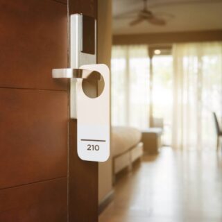 Hotel room door with a white keycard hanging from the handle, room 210 visible in a softly lit hallway.