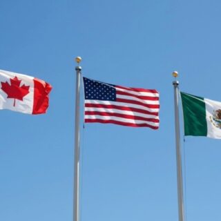 Three national flags—Canada, United States, and Mexico—flying on flagpoles against a clear blue sky.