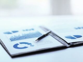 Printed business reports with blue bar and pie charts on a desk, a pen resting on the pages.