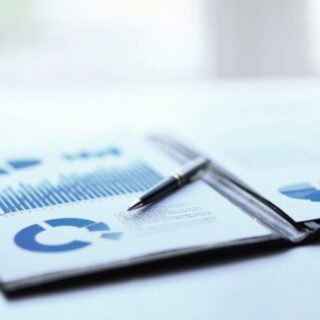 Printed business reports with blue bar and pie charts on a desk, a pen resting on the pages.