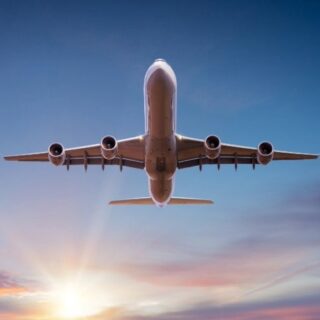 Four-engine commercial airplane seen from below against a sunset sky.