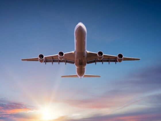 Four-engine commercial airplane seen from below against a sunset sky.