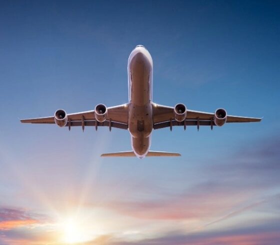 Four-engine commercial airplane seen from below against a sunset sky.