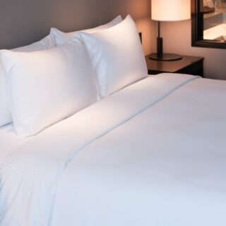 Hotel bed with crisp white sheets and pillows, softly lit bedside lamps visible in the background.