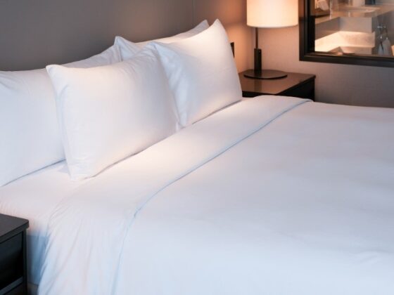 Hotel bed with crisp white sheets and pillows, softly lit bedside lamps visible in the background.