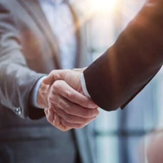 Two business professionals shake hands in a bright office, symbolizing a partnership or agreement.