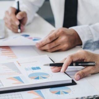 Two professionals review printed charts and graphs on a desk, one pointing with a pen that emphasizes data insights.