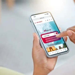 Person holds a smartphone displaying a flight-booking app with a 'Book a Flight' search bar.