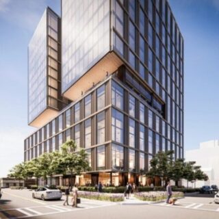 Modern glass office tower with a cantilevered upper floor at a busy street corner, pedestrians and cars nearby.