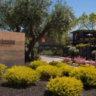 Entrance to Bardessono Hotel & Spa with a stone sign, lush desert landscaping, and a tree-lined path ahead