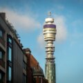 BT Tower rising between city buildings against a blue sky, London landmark visible in the street canyon
