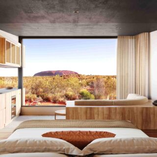 Luxurious bedroom with a large window opening to a desert landscape, warm wood furniture, and neutral textiles.",