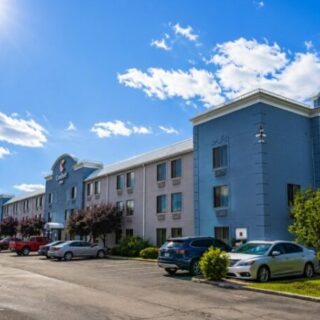 Exterior view of a blue hotel with a curved corner facade and several parked cars on a sunny day