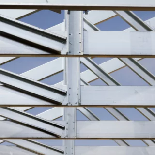 Close-up of silver steel beams and diagonal bracing forming a structural framework against a blue sky.