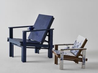 Blue wooden Adirondack chair with a small round table holding a blue teacup; nearby is a white chair with blue floral upholstery.