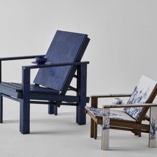 Blue wooden Adirondack chair with a small round table holding a blue teacup; nearby is a white chair with blue floral upholstery.