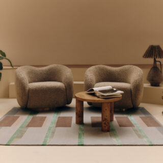 Two plush beige armchairs face each other with a small round wooden table between them in a neutral living room.