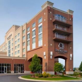 Brick DoubleTree by Hilton hotel exterior with arched entrance and flagpoles by the driveway.