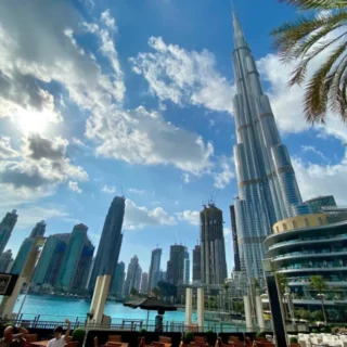 Dubai Marina skyline with the Burj Khalifa beside a waterfront promenade and palm trees on a sunny day
