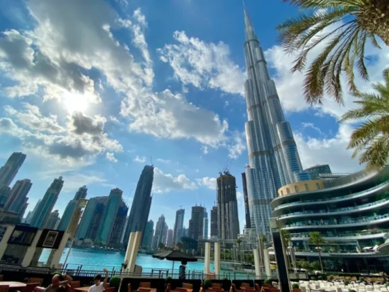 Dubai Marina skyline with the Burj Khalifa beside a waterfront promenade and palm trees on a sunny day