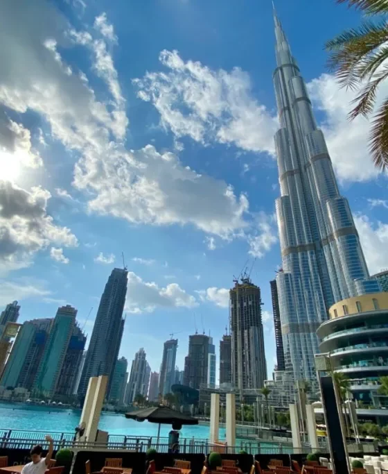 Dubai Marina skyline with the Burj Khalifa beside a waterfront promenade and palm trees on a sunny day