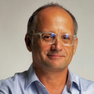 Portrait of a middle-aged man with short gray hair and clear glasses, wearing a light blue shirt.