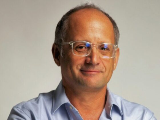 Portrait of a middle-aged man with short gray hair and clear glasses, wearing a light blue shirt.